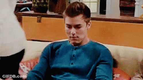 A Man Is Sitting On A Couch Wearing A Blue Shirt GIF