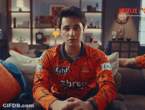 A Man Is Sitting On A Couch Wearing A Shree Shirt GIF