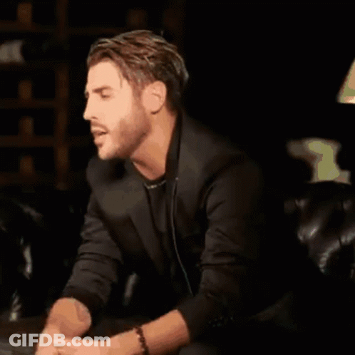 A Man Is Sitting On A Couch Wearing Headphones And A Black Jacket . GIF