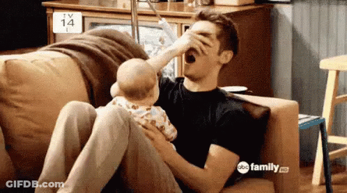 A Man Is Sitting On A Couch With A Baby And Drinking From A Bottle . GIF