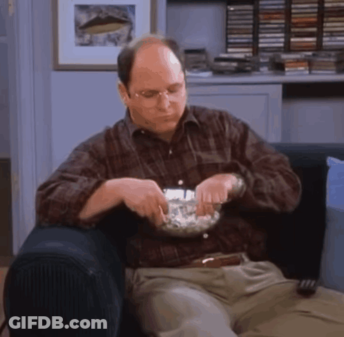 A Man Is Sitting On A Couch With A Bowl Of Popcorn In His Hand . GIF