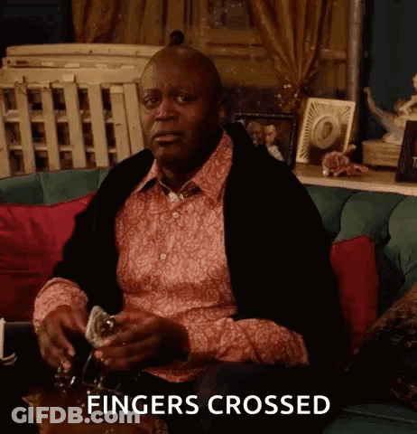 A Man Is Sitting On A Couch With A Glass Of Wine In His Hand And The Words Fingers Crossed Above Him . GIF