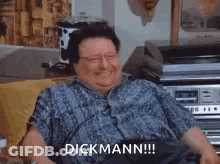A Man Is Sitting On A Couch With A Record Player In The Background And Laughing . GIF