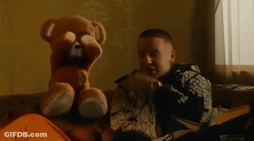 A Man Is Sitting On A Couch With A Teddy Bear Covering His Face . GIF