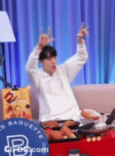 A Man Is Sitting On A Couch With His Arms In The Air And Making A Horn Sign . GIF