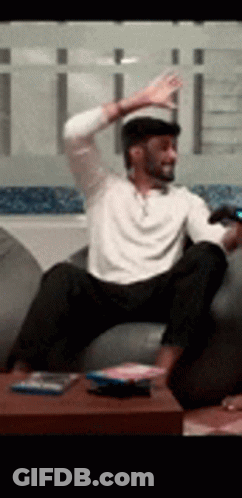 A Man Is Sitting On A Couch With His Arms In The Air . GIF