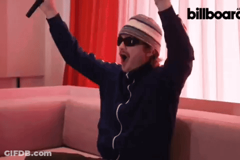 A Man Is Sitting On A Couch With His Arms In The Air In Front Of A Billboard Ad GIF