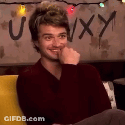 A Man Is Sitting On A Couch With His Hand To His Mouth And A Sign In The Background That Says Uxy . GIF