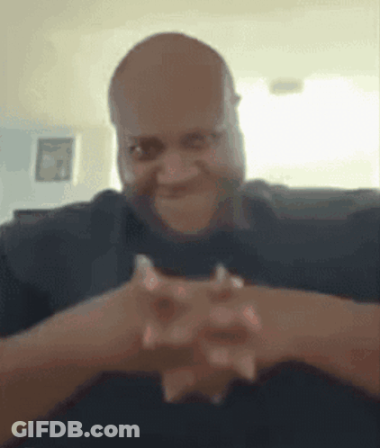 A Man Is Sitting On A Couch With His Hands Folded In Front Of His Face . GIF