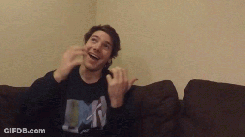 A Man Is Sitting On A Couch With His Hands In The Air And Wearing A Shirt That Says Mtv . GIF