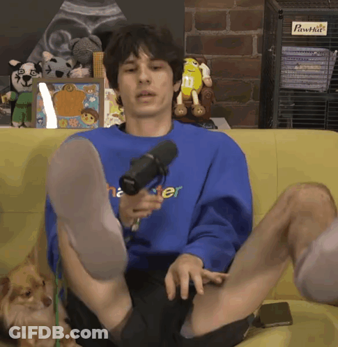 A Man Is Sitting On A Couch With His Legs Crossed Wearing A Blue Shirt That Says Master GIF