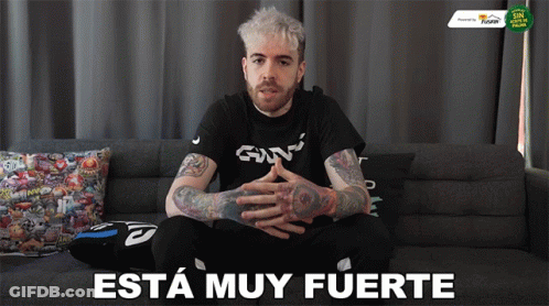 A Man Is Sitting On A Couch With The Words " Esta Muy Fuerte " Written On The Bottom GIF
