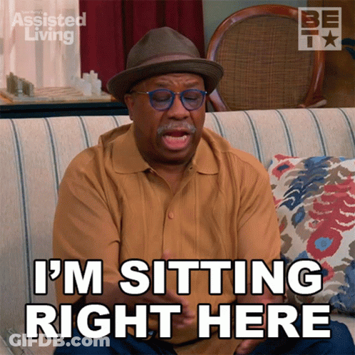A Man Is Sitting On A Couch With The Words I 'M Sitting Right Here GIF
