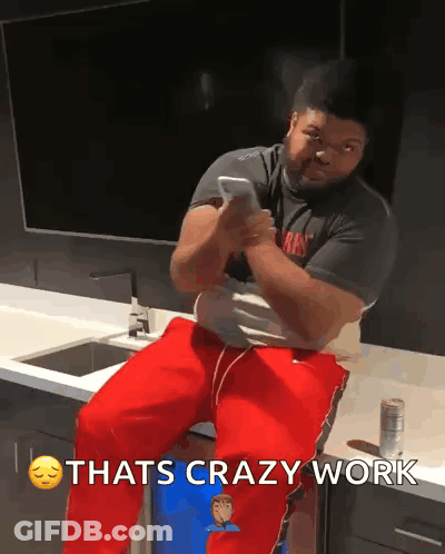 A Man Is Sitting On A Counter Looking At His Phone With The Words Thats Crazy Work Above Him GIF