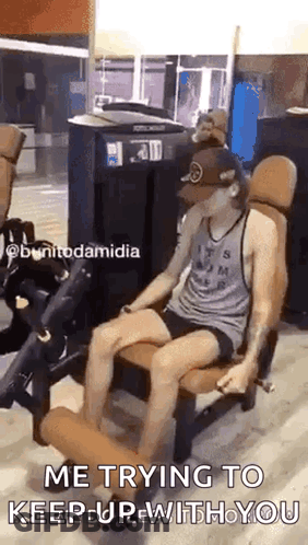 A Man Is Sitting On A Leg Extension Machine In A Gym And Says `` Me Trying To Keep Up With You '' . GIF