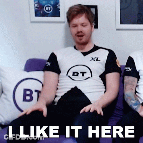 A Man Is Sitting On A Purple Couch With The Words I Like It Here On The Bottom GIF