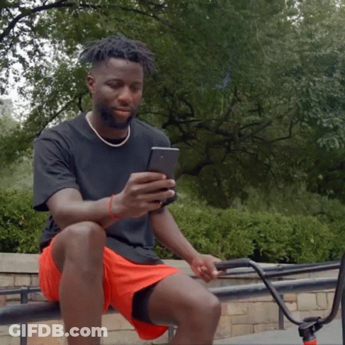 A Man Is Sitting On A Railing Looking At His Phone GIF