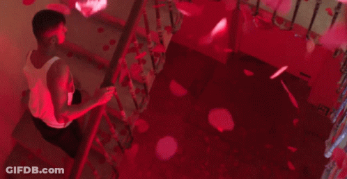 A Man Is Sitting On A Set Of Stairs With Petals Falling From The Ceiling . GIF