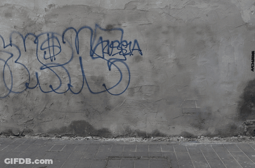 A Man Is Sitting On A Skateboard On A Wall With Graffiti On It That Says Destroy GIF