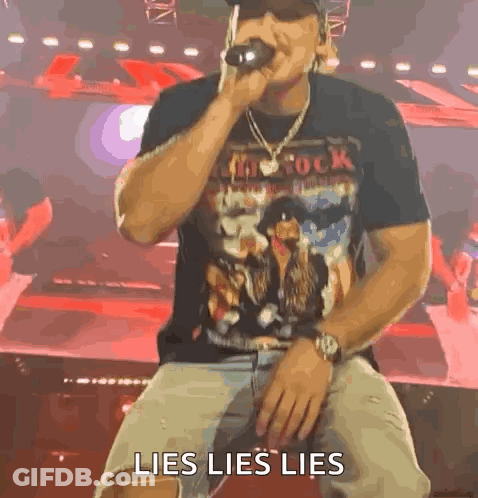 A Man Is Sitting On A Stage Singing Into A Microphone With The Words Lies Lies Lies Written On The Screen Behind Him . GIF