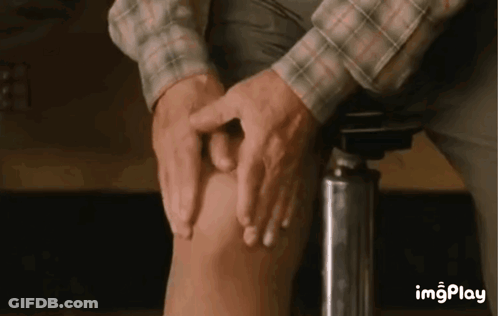 A Man Is Sitting On A Stool And Touching His Knee With His Hands . GIF