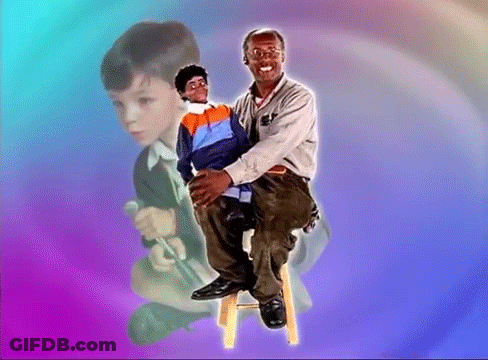 A Man Is Sitting On A Stool Holding A Puppet In His Lap GIF
