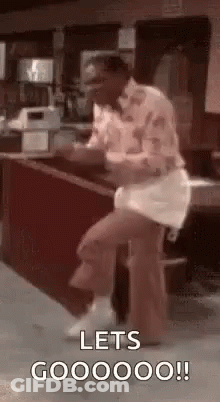 A Man Is Sitting On A Stool In Front Of A Counter And Dancing . GIF