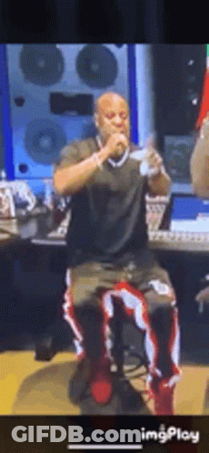 A Man Is Sitting On A Stool Singing Into A Microphone In A Recording Studio . GIF