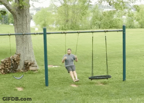 A Man Is Sitting On A Swing In A Park . GIF