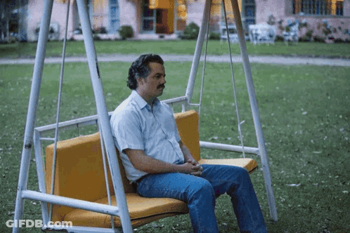 A Man Is Sitting On A Swing In The Grass GIF
