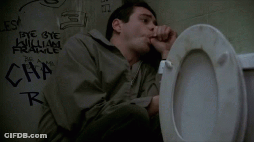 A Man Is Sitting On A Toilet In A Bathroom With Graffiti On The Wall Behind Him . GIF