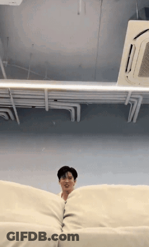 A Man Is Sitting On A White Couch In A Room With A Ceiling Fan . GIF