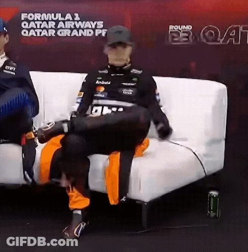 A Man Is Sitting On A White Couch In Front Of A Sign That Says Formula 1 Qatar Airways GIF