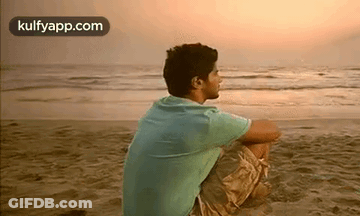 A Man Is Sitting On The Beach And Looking At The Ocean . GIF