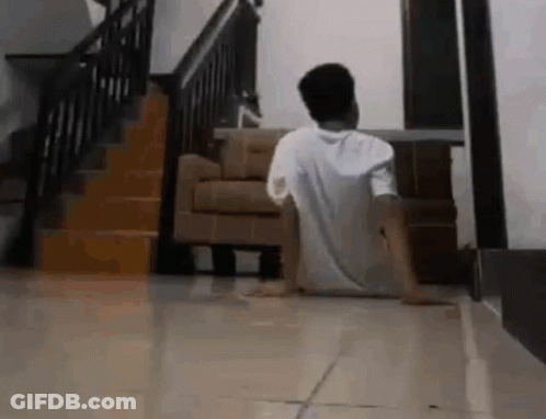 A Man Is Sitting On The Floor In A Living Room In Front Of A Staircase . GIF