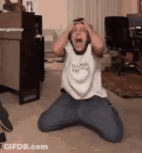 A Man Is Sitting On The Floor With His Hands On His Head . GIF