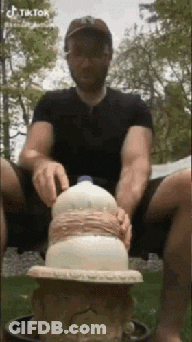 A Man Is Sitting On The Ground With A Milk Bottle On Top Of Him . GIF