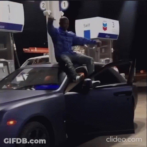 A Man Is Sitting On The Hood Of A Car At A Gas Station GIF