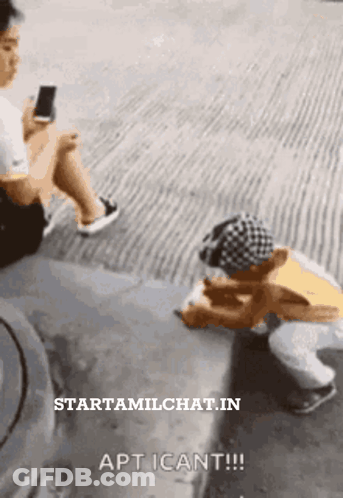 A Man Is Sitting On The Side Of The Road Looking At A Cell Phone GIF