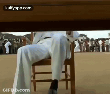 A Man Is Sitting Under A Table With His Legs Crossed . GIF