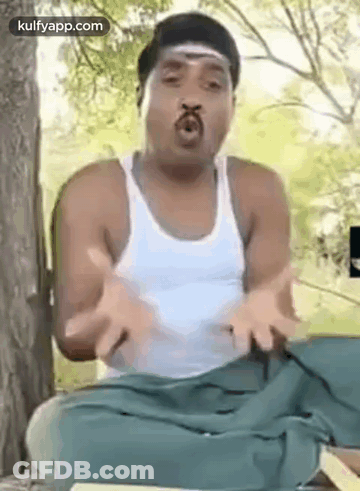 A Man Is Sitting Under A Tree With His Hands Outstretched And Making A Funny Face . GIF