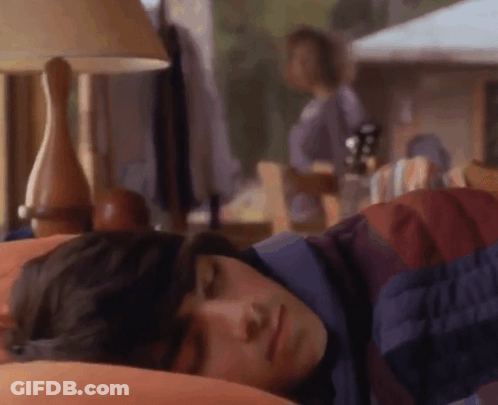 A Man Is Sleeping In A Bed With A Lamp And A Woman Standing In The Background . GIF