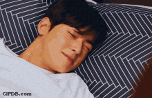 A Man Is Sleeping In A Bed With A Striped Pillow And A White Blanket . GIF