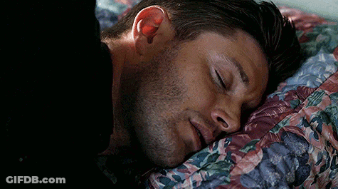 A Man Is Sleeping In A Bed With His Eyes Closed And A Floral Blanket . GIF