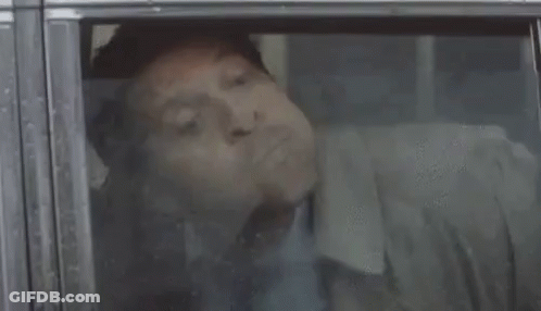 A Man Is Sleeping In A Car With His Mouth Open And His Tongue Sticking Out . GIF