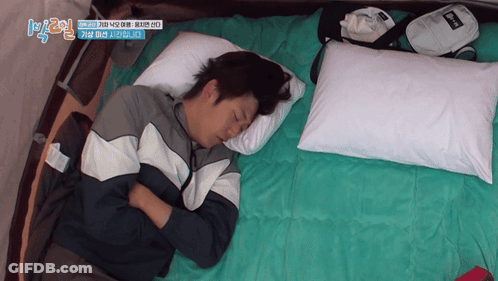 A Man Is Sleeping On A Bed With A Bag That Says ' Reebok ' On It GIF