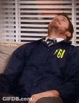A Man Is Sleeping On A Couch Wearing A Fbi Jacket And Tie . GIF