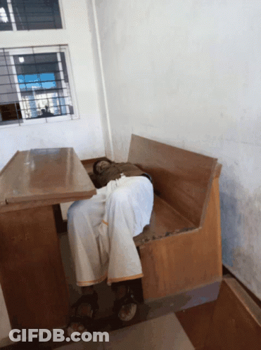 A Man Is Sleeping On A Wooden Bench In A Room GIF