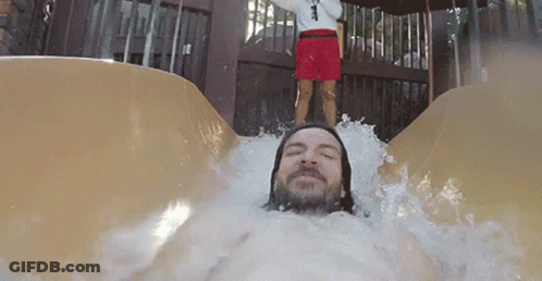 A Man Is Sliding Down A Water Slide With A Lifeguard Standing Behind Him GIF