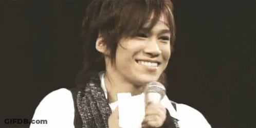 A Man Is Smiling And Holding A Microphone In His Hand . GIF